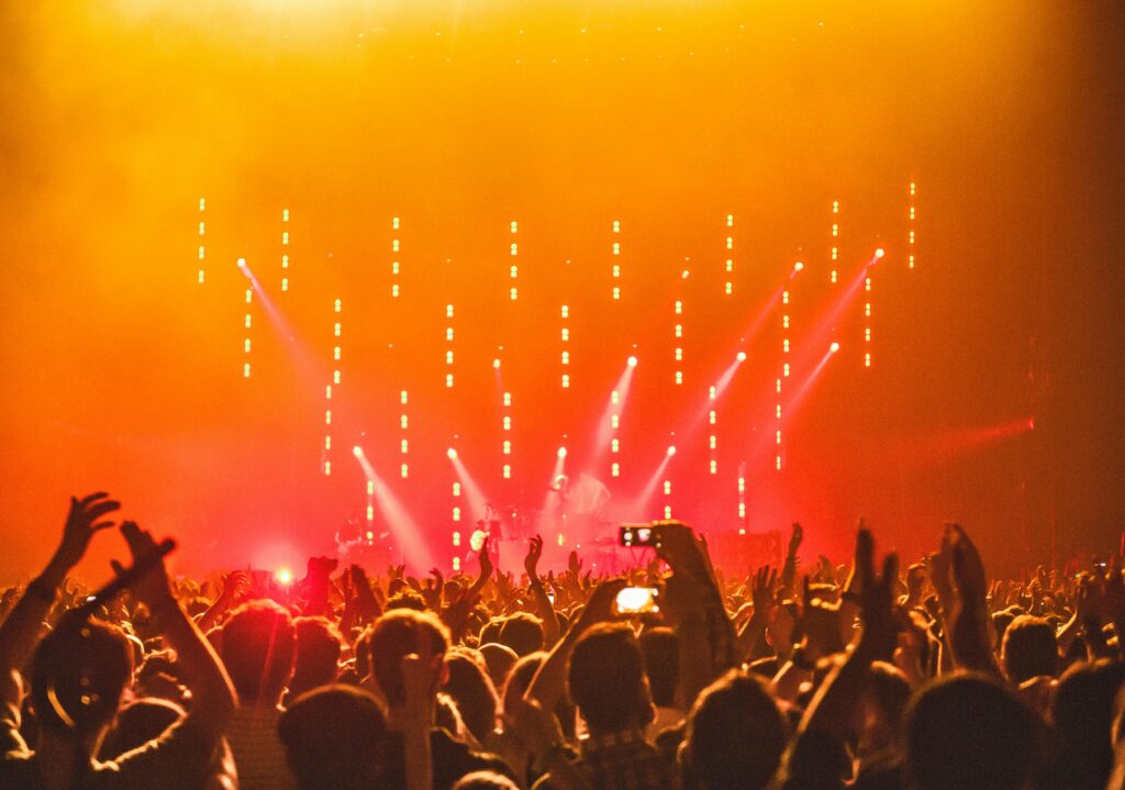 Energetic crowd at a live concert with bright stage lights and hands raised in celebration.